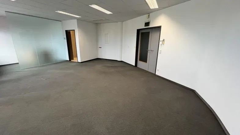 Geräumiger, leerer Büroraum mit Teppichboden und Glastrennwänden, bereit für die individuelle Gestaltung.
