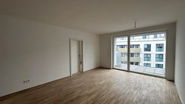Helles, unmöbliertes Wohnzimmer mit Holzboden und Zugang zu einem Balkon.