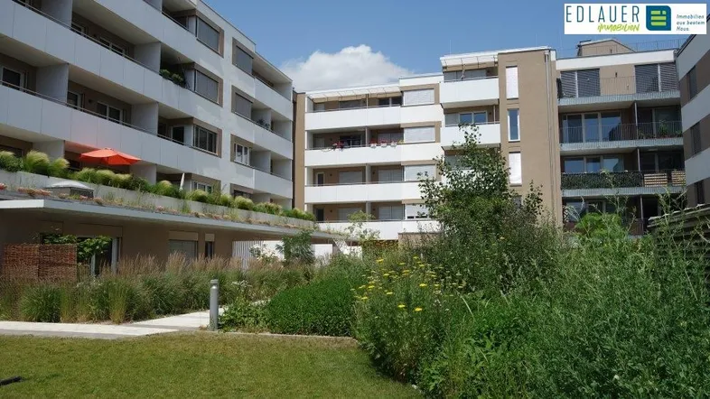 Moderne Wohnanlage mit begrüntem Innenhof und Balkonen unter blauem Himmel.
