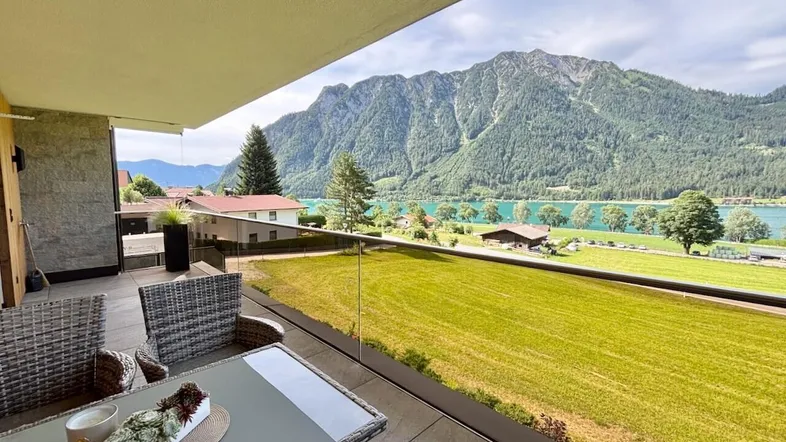 Möblierter Balkon mit Glasgeländer und atemberaubendem Blick auf den See und die Berge.