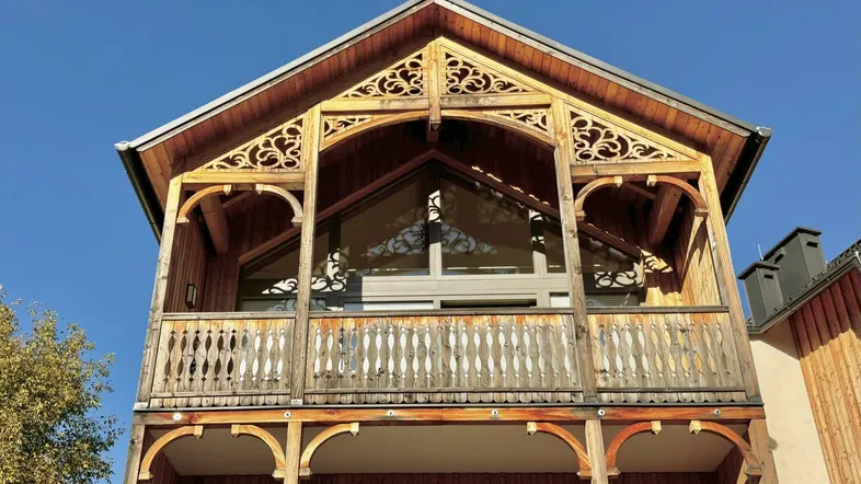 Traditionelle Holzfassade mit kunstvoll geschnitzten Balkongeländern und Giebelverzierungen unter blauem Himmel.