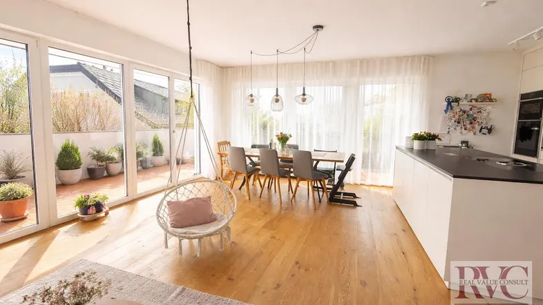 Heller, offener Wohn- und Essbereich mit moderner Küche, Holzboden und Zugang zur sonnigen Terrasse.