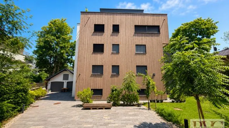 Modernes Mehrfamilienhaus mit Holzfassade und gepflasterter Zufahrt unter blauem Himmel.