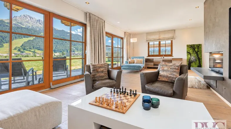 Helles Wohnzimmer mit Holzboden, Kamin und großen Fenstern mit Bergblick.