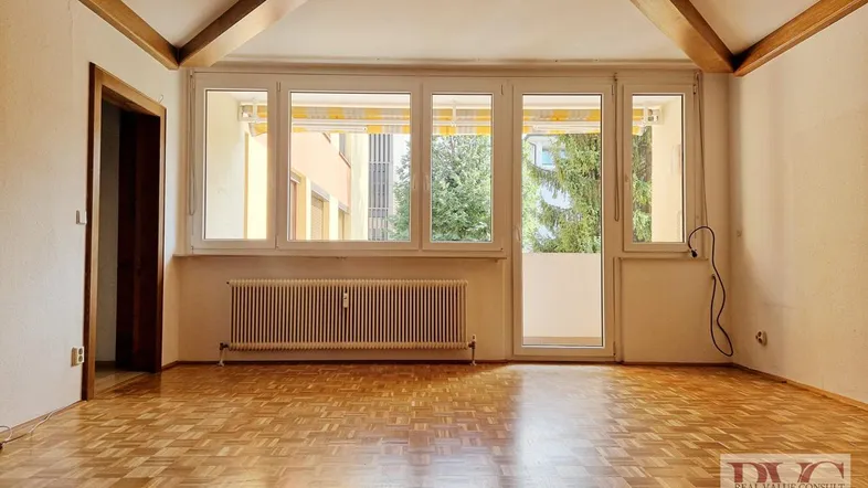 Helles Wohnzimmer mit Parkettboden, Holzbalkendecke und Zugang zum Balkon.