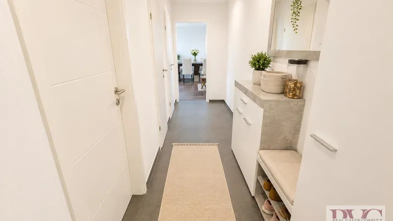 Helle Diele mit modernem Schuhschrank, Spiegel und dunklem Fliesenboden.