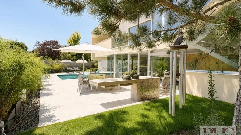 Großzügige Terrasse mit Essbereich, Sonnenschirm und Pool, umgeben von Grünflächen und Bäumen.