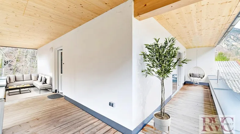 Geräumiger, überdachter Balkon mit Holzboden, Sitzgelegenheiten und Blick ins Grüne.