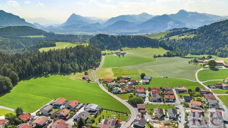 Luftaufnahme eines malerischen Dorfes in einer grünen Tallandschaft mit majestätischen Bergen im Hintergrund.