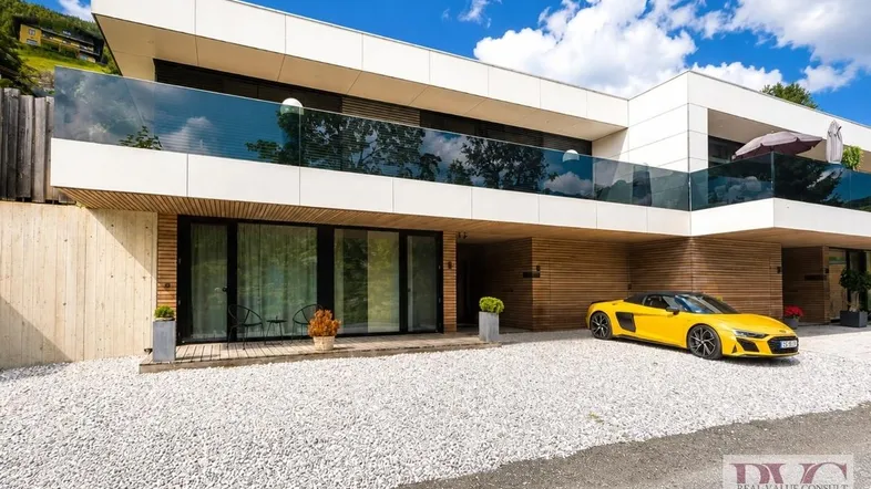 Moderne Architektur mit weißer Fassade, Holzverkleidung und großzügigen Glasfronten, inklusive einer Einfahrt.