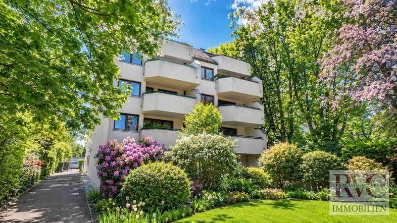 Mehrfamilienhaus umgeben von blühenden Bäumen und einer gepflegten Gartenanlage.