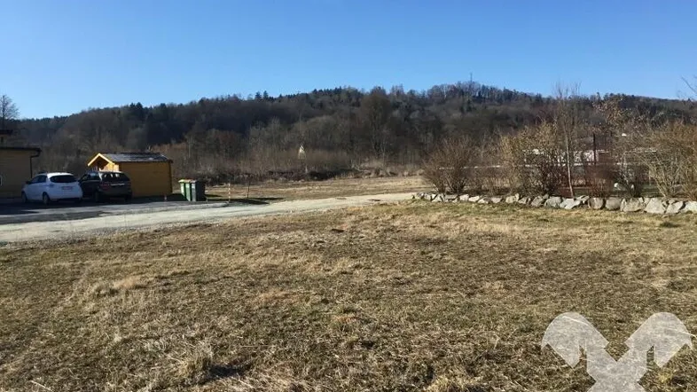 Weitläufiges Grundstück mit Blick auf bewaldete Hügel und einige entfernte Gebäude unter blauem Himmel.