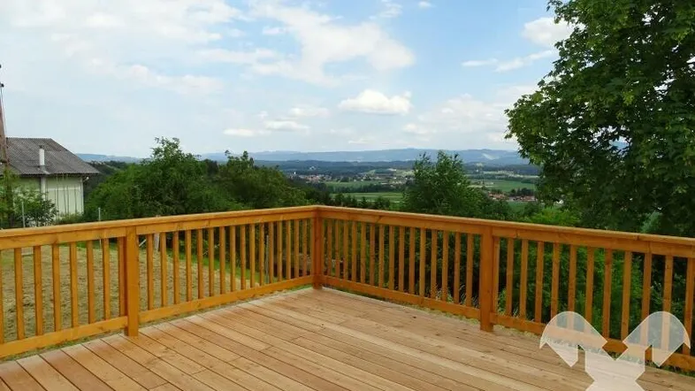 Geräumige Holzterrasse mit weitem Blick über die grüne Landschaft und den Horizont.