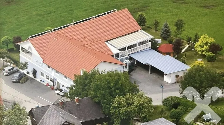 Luftaufnahme eines großen Gebäudes mit rotem Ziegeldach, Carport und Spielplatz in ländlicher Umgebung.