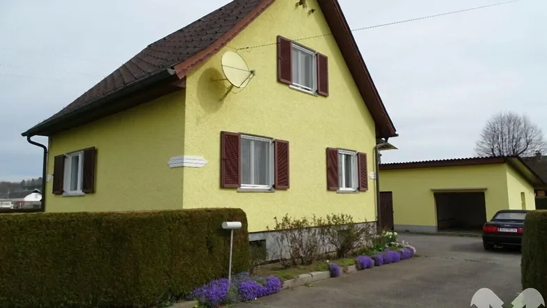Gelbes Einfamilienhaus mit braunen Fensterläden, Vorgarten und separater Garage.
