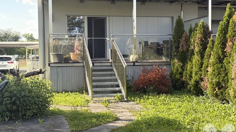 Terrasse mit Glasgeländer und Treppe, die zum grünen Gartenbereich des Hauses führt.