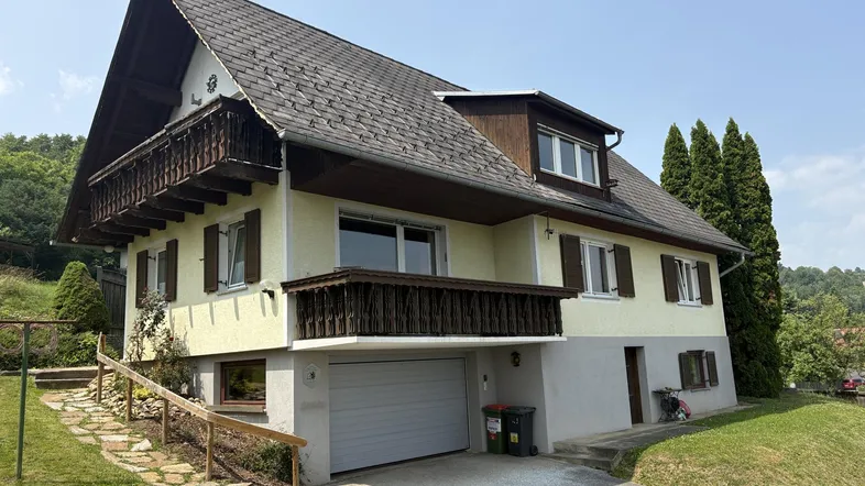 Traditionelles Haus mit Satteldach, Balkonen und integrierter Garage in ländlicher Umgebung.