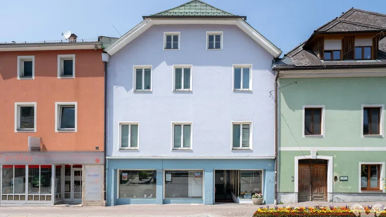 Vorderansicht eines historischen Gebäudes mit hellblauer Fassade und Geschäftsräumen im Erdgeschoss.