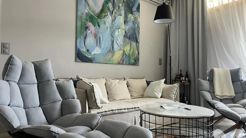 Helles Wohnzimmer mit modernen Sesseln, Sofa, großem Kunstwerk und Klimaanlage.