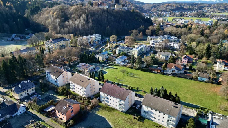 Luftaufnahme einer Wohnsiedlung mit grünen Flächen, umgeben von Hügeln und einem historischen Gebäude.