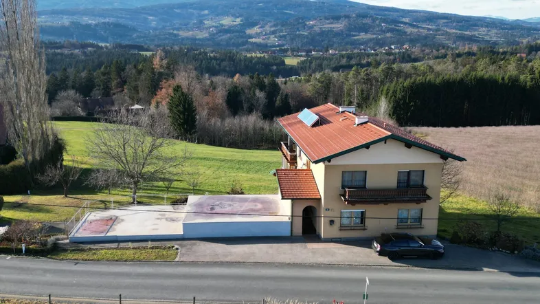 Großzügiges Einfamilienhaus mit rotem Ziegeldach und Photovoltaikanlage in ländlicher Umgebung mit Bergblick.