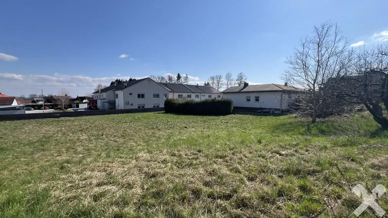 Weitläufiges Grundstück mit Grasfläche und Blick auf umliegende Wohnhäuser unter blauem Himmel.