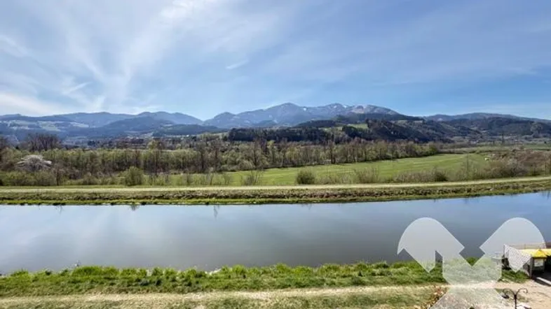 Panoramablick vom Balkon auf den Fluss und die umliegenden Berge unter blauem Himmel.