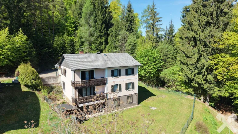 Hausfassade mit mehreren Balkonen und umgeben von üppiger Natur und Wald.