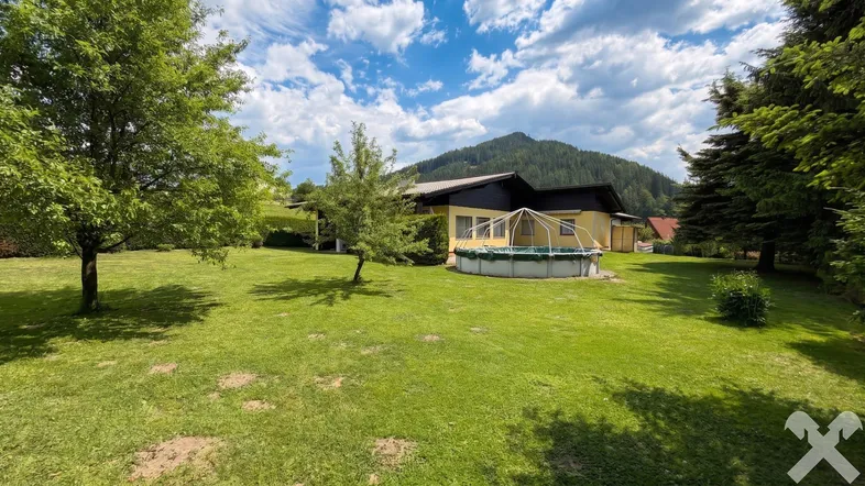 Großer grüner Garten mit Rasenfläche, Bäumen, einem Aufstellpool und Bergblick.