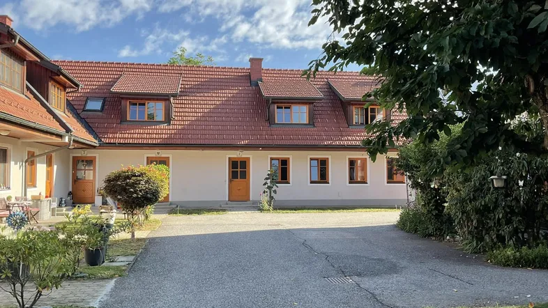 Traditionelles Gebäude mit rotem Ziegeldach und gepflasterter Zufahrt, umgeben von Grünflächen.