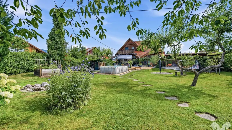 Weitläufiger grüner Garten mit Rasenfläche, Bäumen und einem kleinen Pool im Hintergrund.