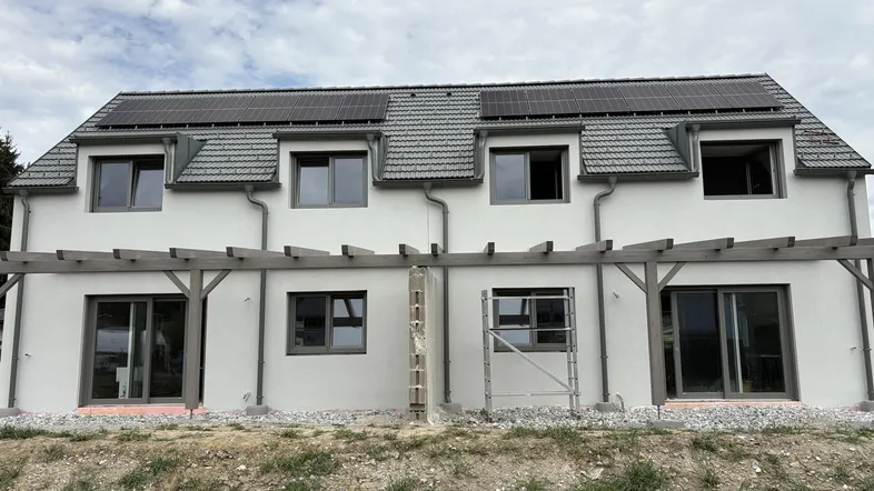 Neubau-Doppelhaushälfte mit Solarpaneelen auf dem Dach und Pergola-Struktur im Bau.