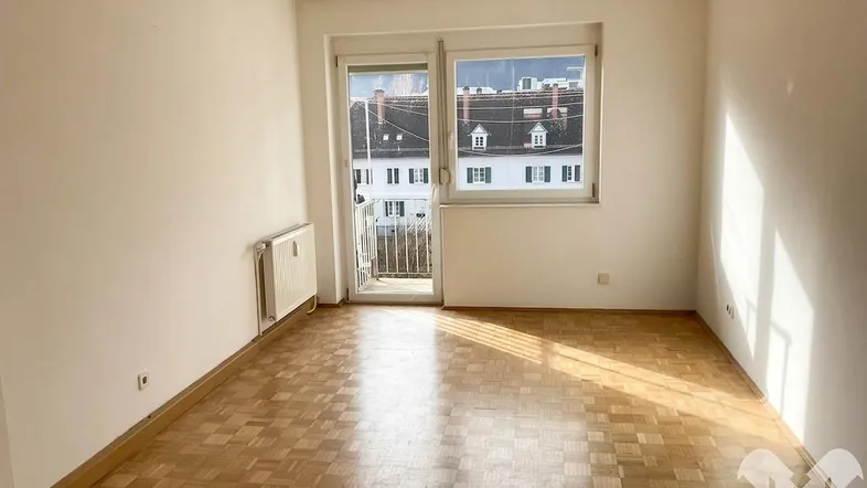 Helles Zimmer mit Parkettboden und Zugang zu einem kleinen Balkon, ideal als Wohn- oder Schlafzimmer.