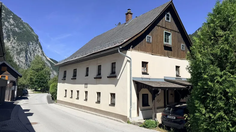 Traditionelles Haus in den Bergen mit weißer Fassade und Holzelementen unter blauem Himmel.