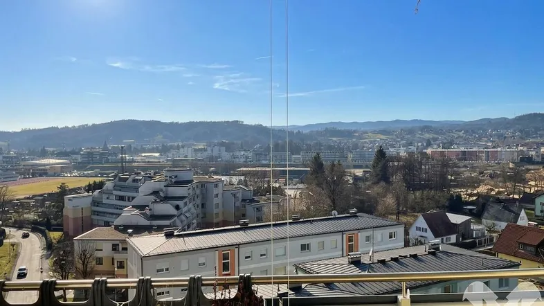 Panoramablick vom Balkon über die Stadt und die umliegende Hügellandschaft an einem sonnigen Tag.