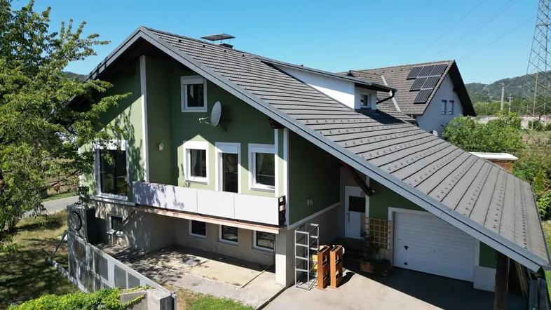 Hausansicht von oben mit grün gestrichener Fassade, Satteldach und Solarpaneelen.
