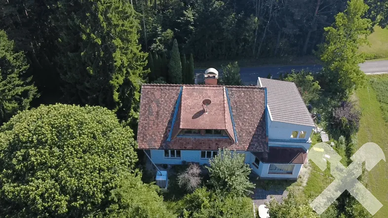 Luftaufnahme eines Hauses mit rotem Ziegeldach, umgeben von dichtem Grün und Bäumen.