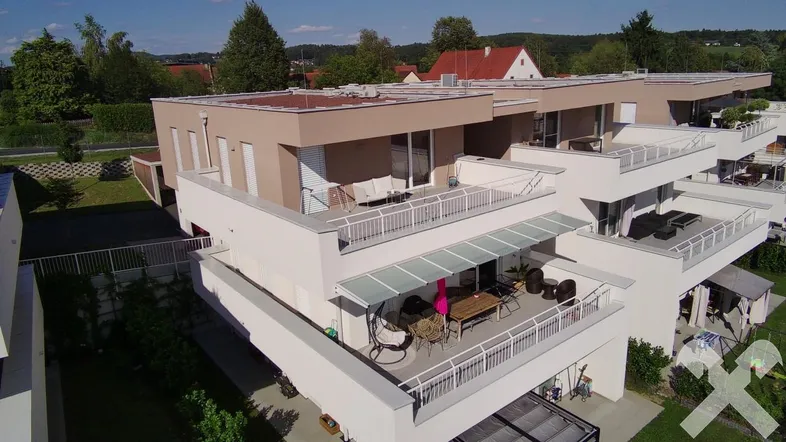 Moderne Wohnanlage mit mehreren Gebäuden, Balkonen und Terrassen in grüner Umgebung.