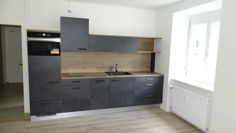 Moderne Küche mit dunklen Schränken, Holzakzenten und integriertem Backofen, hell und funktional gestaltet.