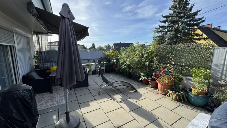 Geräumige Terrasse mit Steinplatten, Gartenmöbeln und vielen Pflanzen unter blauem Himmel.