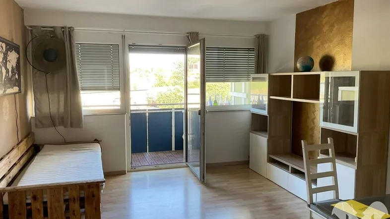 Helles Wohnzimmer mit Holzboden, integriertem Bett und Zugang zu einem sonnigen Balkon.