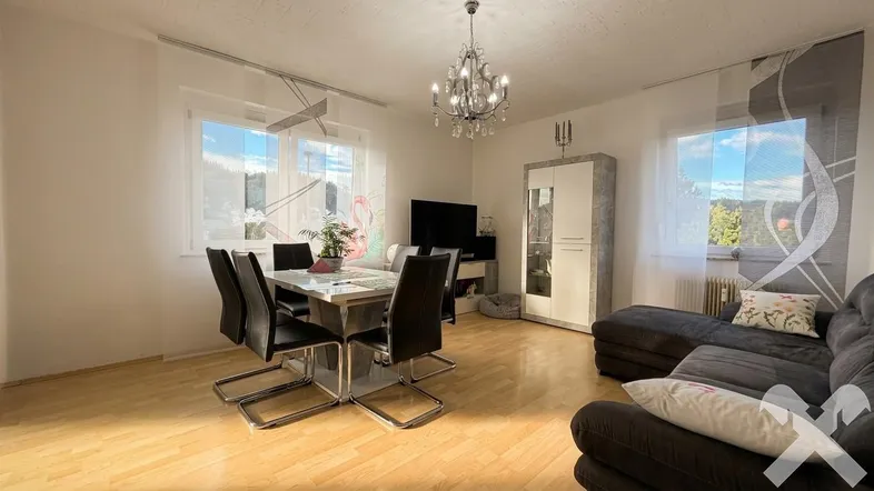Helles Wohn-Esszimmer mit Holzboden, Esstisch und gemütlicher Sofaecke unter einem Kronleuchter.