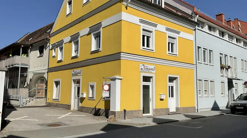 Gelbes Gebäude mit weißer Fassadenverzierung und mehreren Fenstern an einer sonnigen Straße.