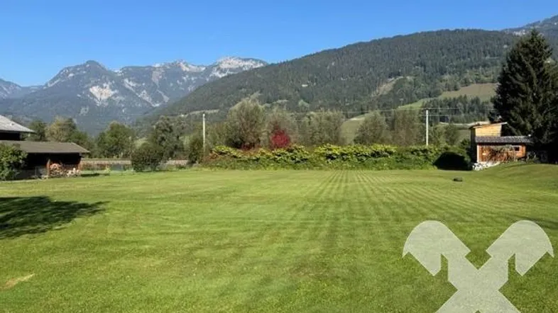 Weitläufige grüne Wiese mit beeindruckendem Bergblick und umliegender Natur unter blauem Himmel.