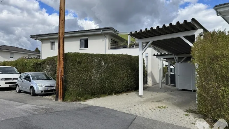 Außenansicht eines Wohnhauses mit Carport, gepflegter Hecke und gepflasterter Einfahrt.