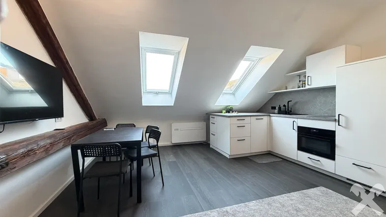 Helle Dachgeschosswohnung mit offener Küche, Essbereich und sichtbaren Holzbalken unter den Dachfenstern.