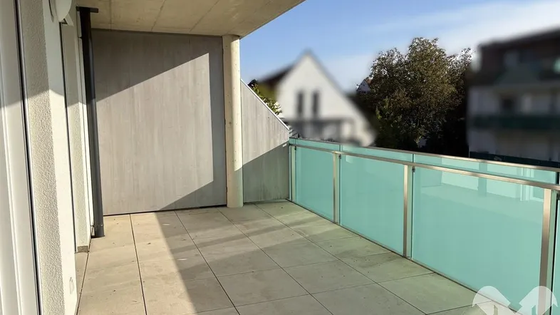 Heller Balkon mit Fliesenboden und moderner Glasbrüstung, ideal für sonnige Stunden im Freien.