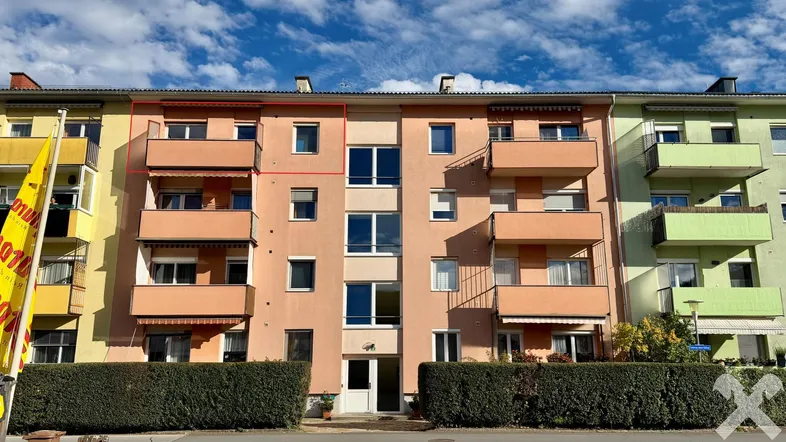 Fassade eines Mehrfamilienhauses mit Balkonen und gepflegter Hecke im Vordergrund.