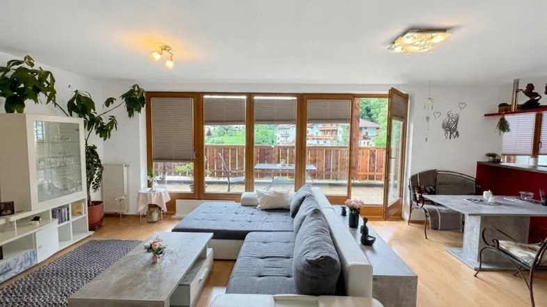 Helles Wohnzimmer mit großem Sofa, Holzboden und Zugang zu einem Balkon mit Bergblick.