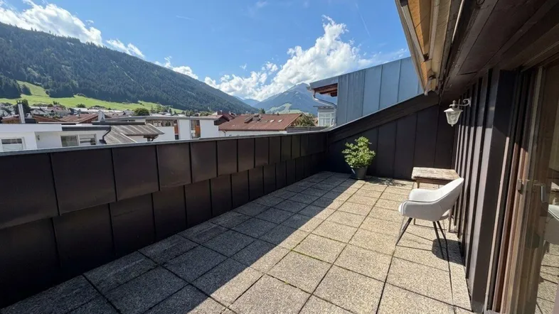 Geräumige Terrasse mit Fliesenboden, Sitzgelegenheit und weitem Bergblick unter blauem Himmel.